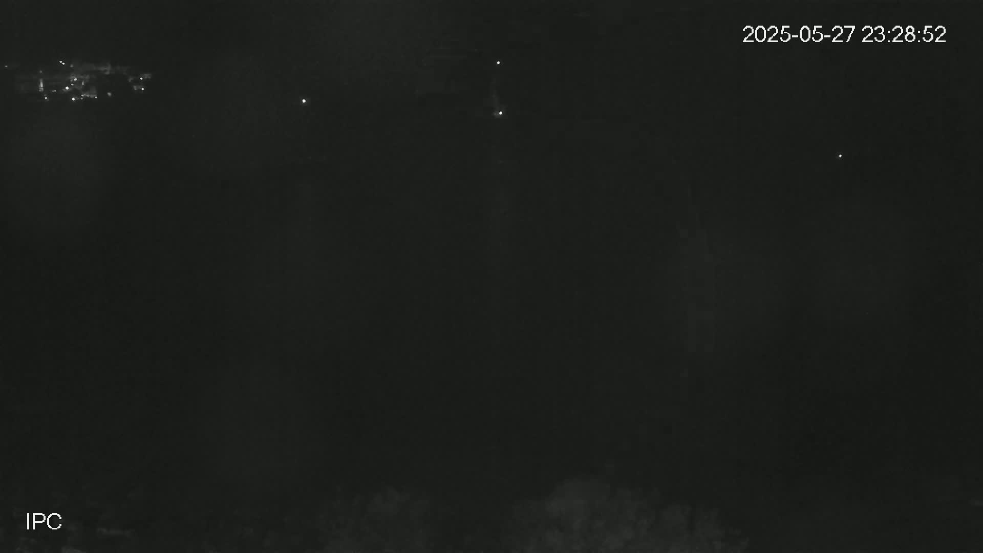 A nighttime, dark image shows a few distant lights in the upper left and a few scattered pinpricks of light across the dark sky.