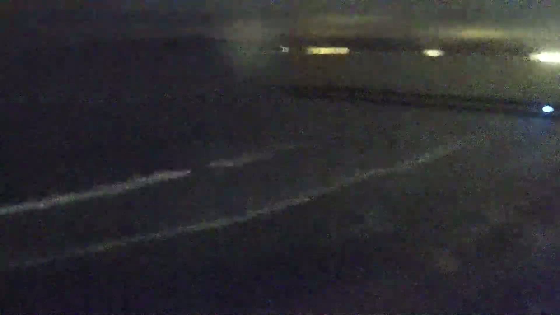 A blurry nighttime image shows two faintly visible white lines on a dark surface, possibly a road, with distant yellow lights in the background.
