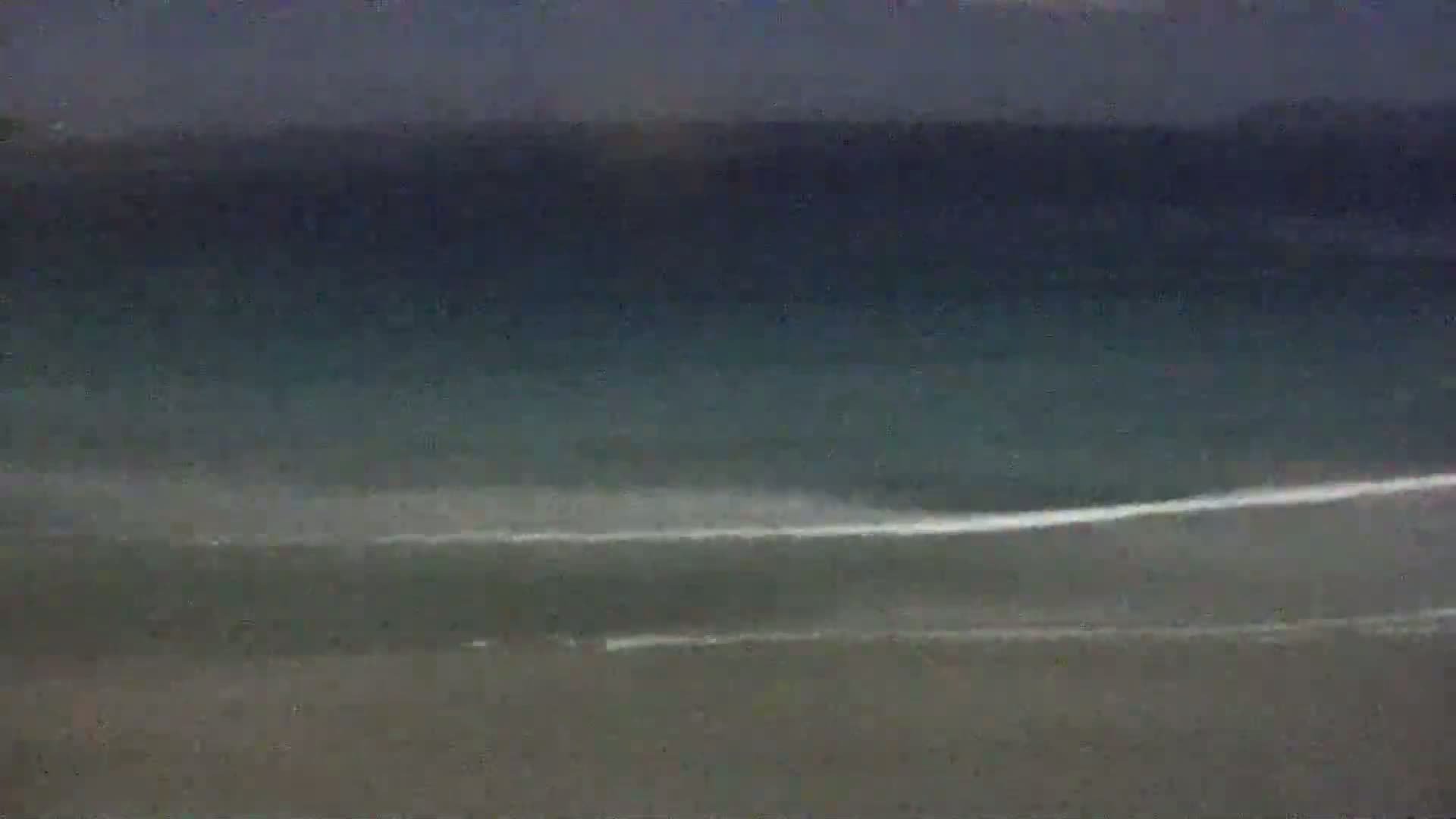 A dark, overcast sky hangs over a mostly calm ocean with small waves breaking near a sandy shore.