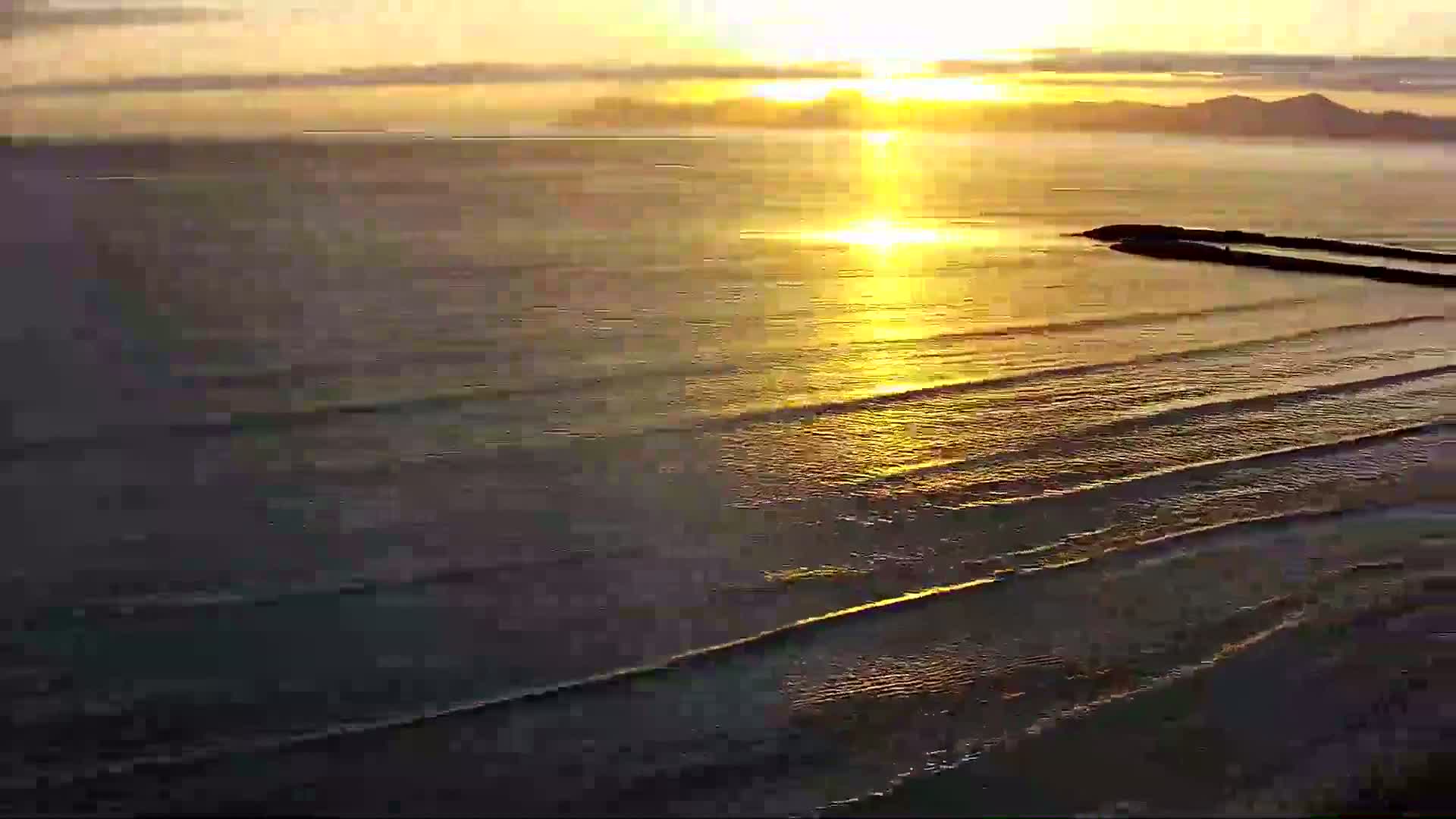 Gentle waves lap a shoreline at sunset, casting a golden light across the water.