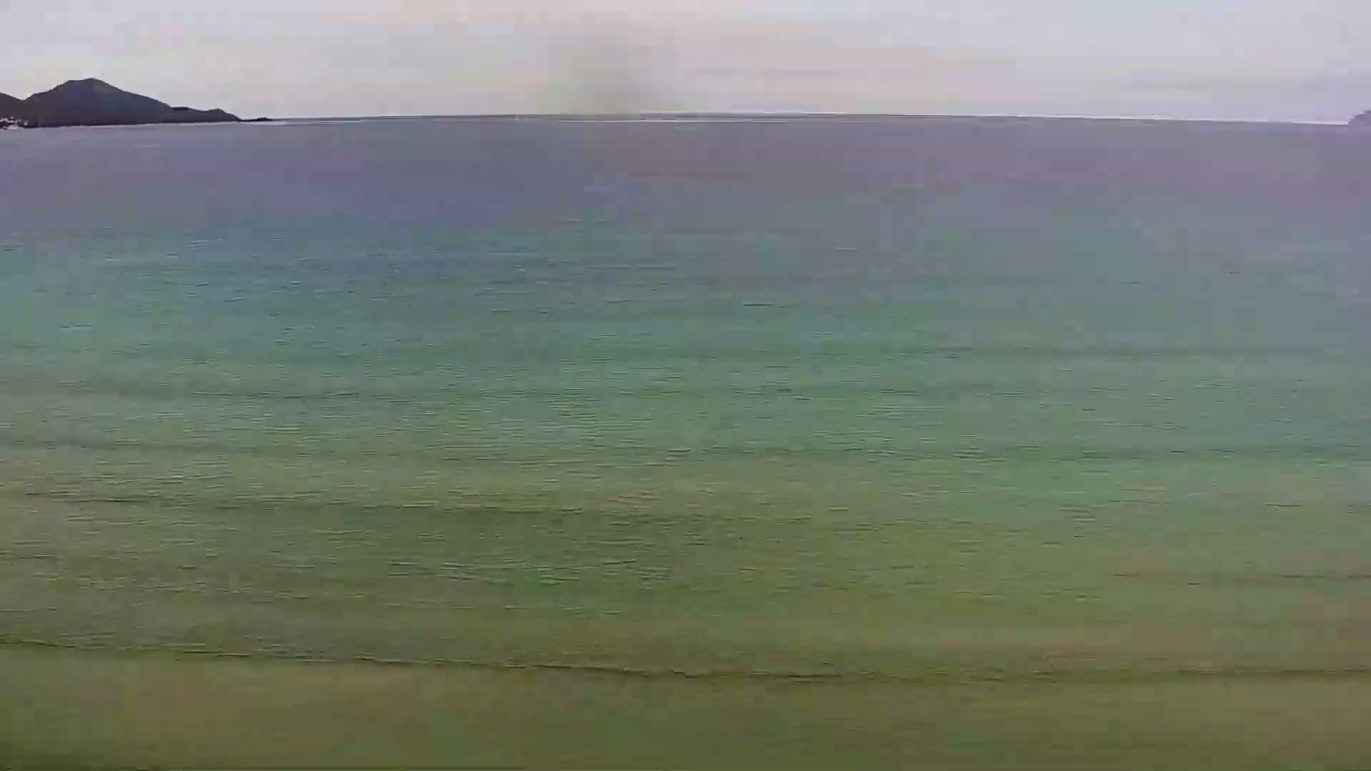 A calm, overcast day shows a tranquil body of water with a distant shoreline.