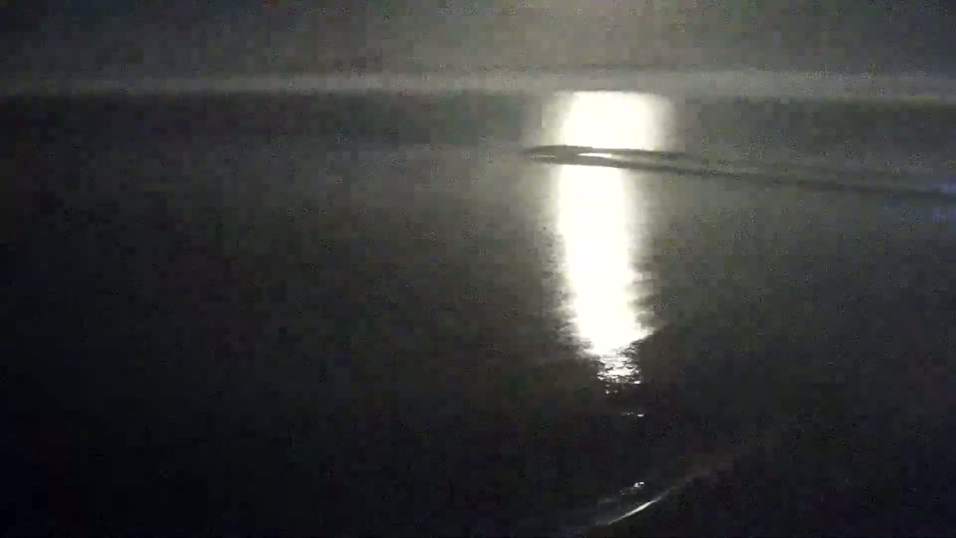 A bright light reflects on dark water at night.