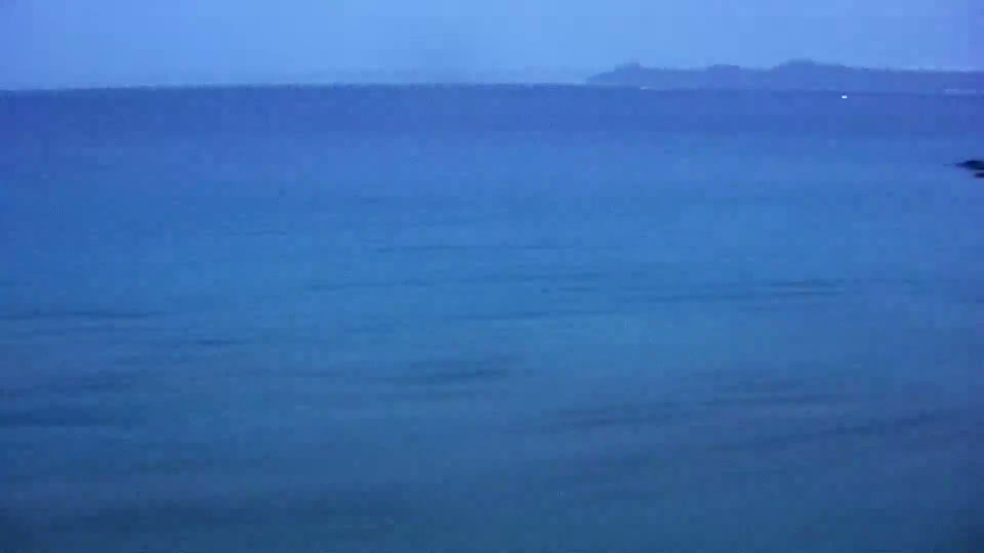 A calm, blue ocean stretches to a distant, hazy shoreline under a dusky sky.