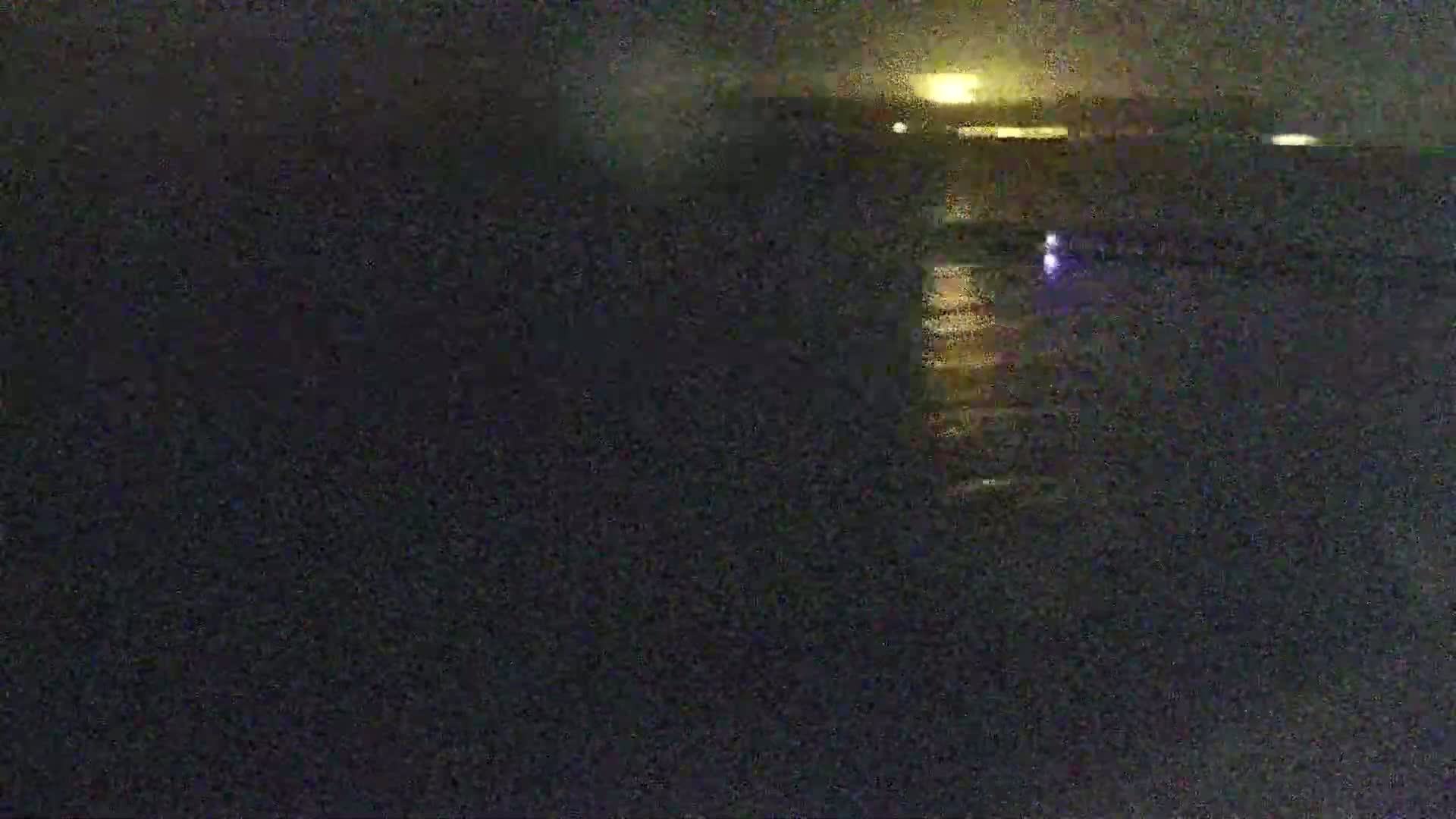 A dark, nighttime scene shows a body of water reflecting faint lights from a distant shoreline.