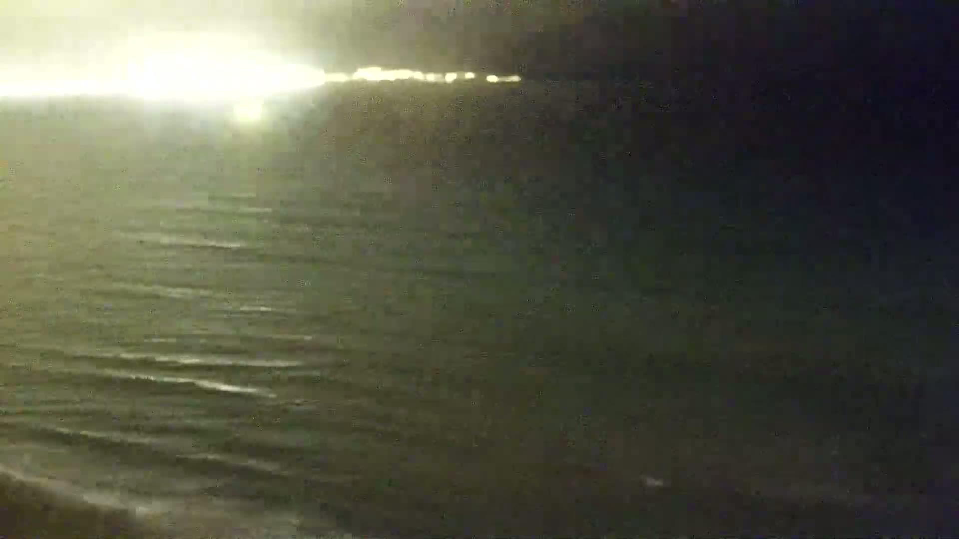 A nighttime view of a calm ocean with faintly visible lights on the horizon.