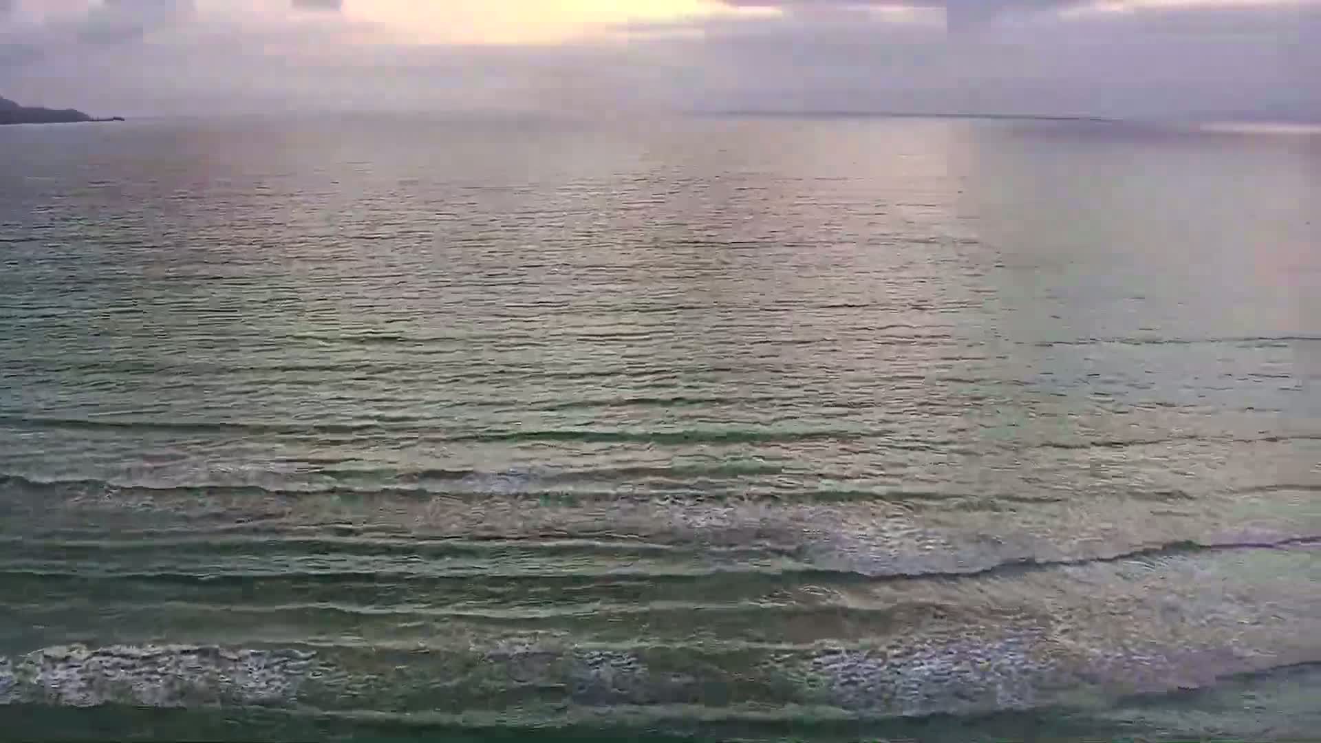 A calm sea with small waves rolls toward the shore under an overcast sky.