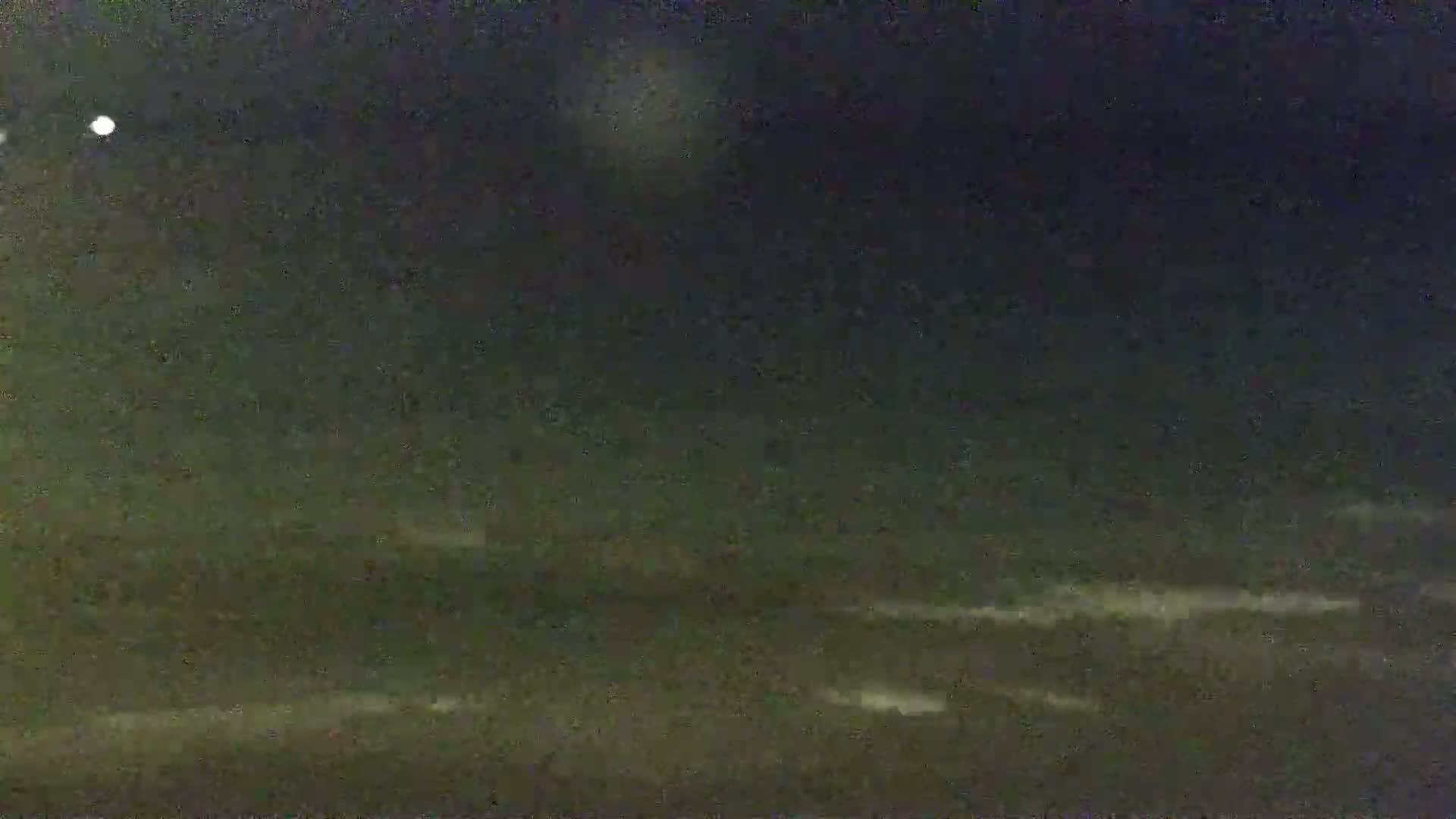 A dark, nighttime scene shows a body of water with subtle wave action under a mostly clear sky.