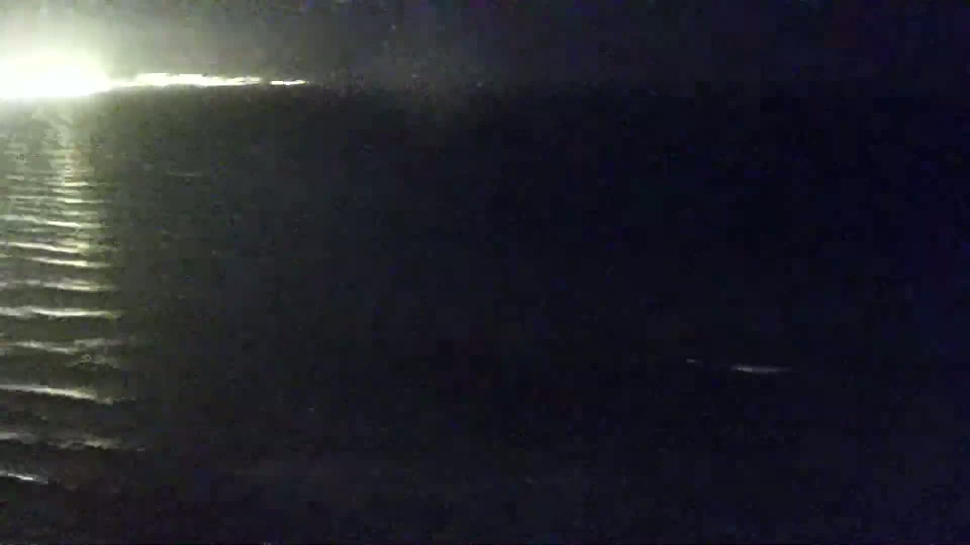 A dark body of water with small waves is visible under a dark night sky, with a bright light source visible in the distance on the left.