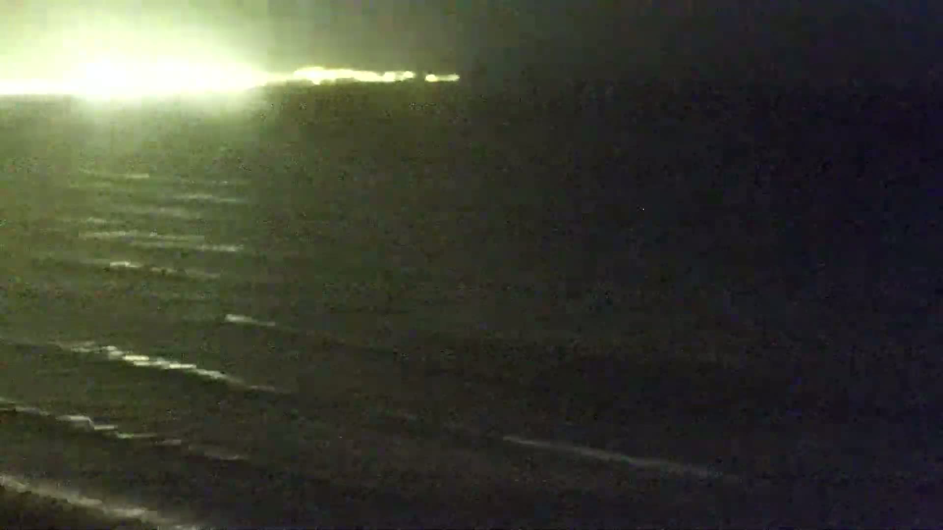 A nighttime view of a dark ocean with gently rolling waves under a bright, yellowish-green sky.