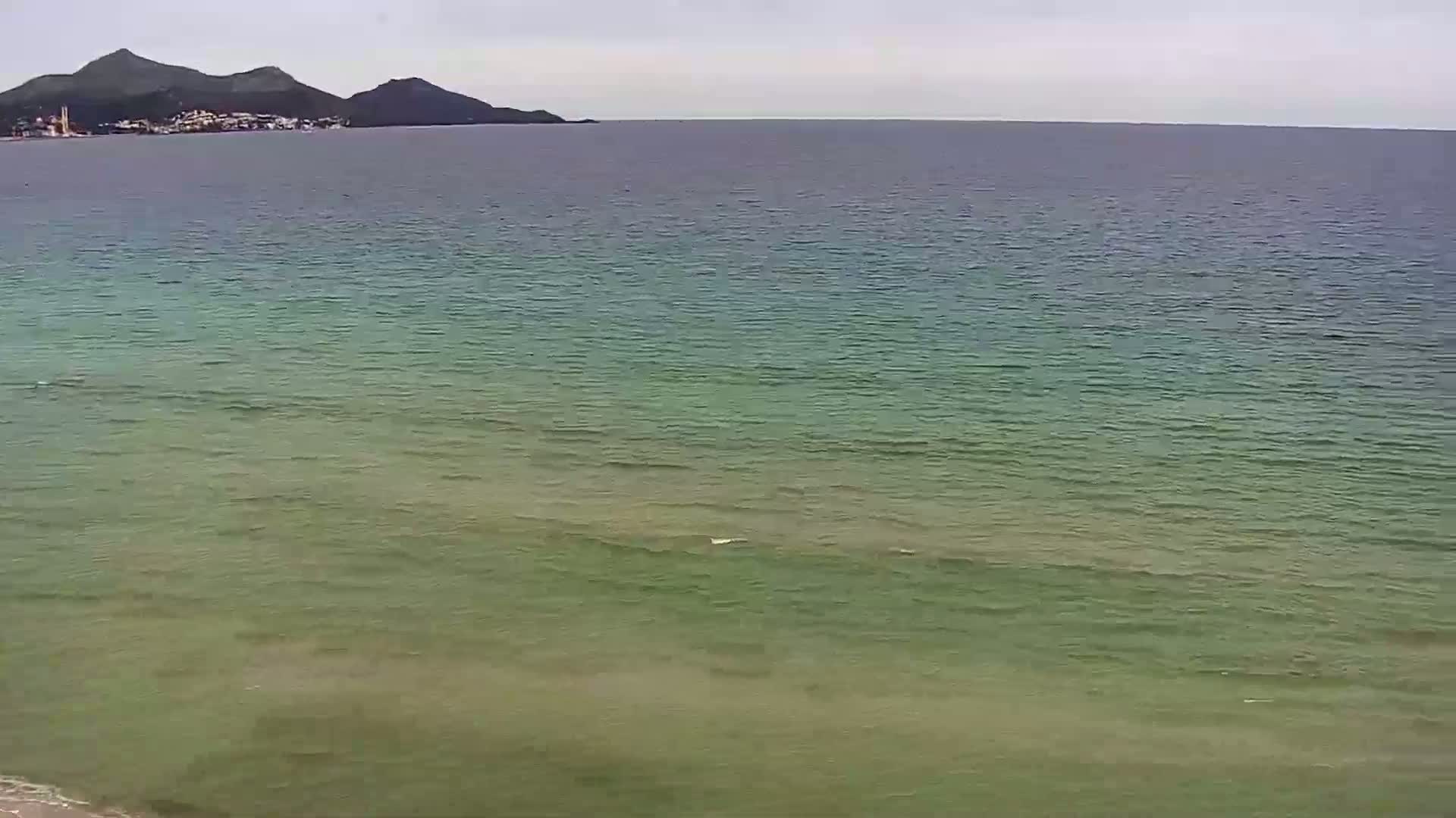 A calm, greenish-blue sea stretches to a distant coastline featuring low mountains under an overcast sky.