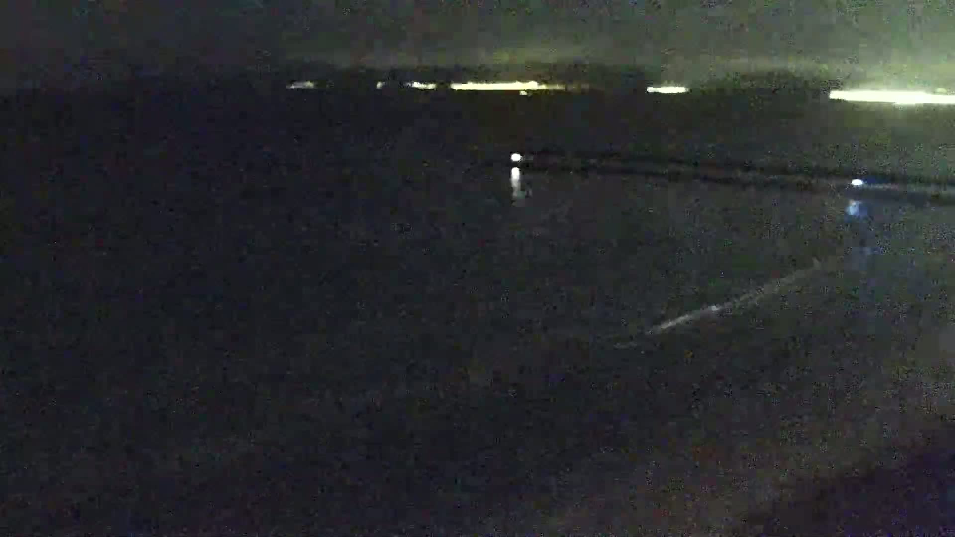 A dark, nighttime view of a body of water with a distant line of lights on the horizon.