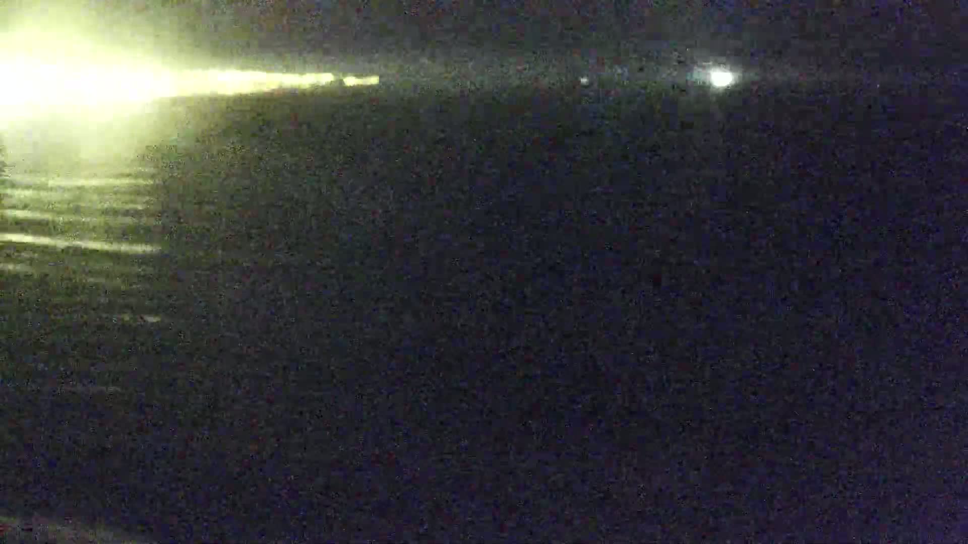 A nighttime, low-light image shows a bright light source in the distance, possibly headlights, reflecting on a dark, possibly wet, surface.