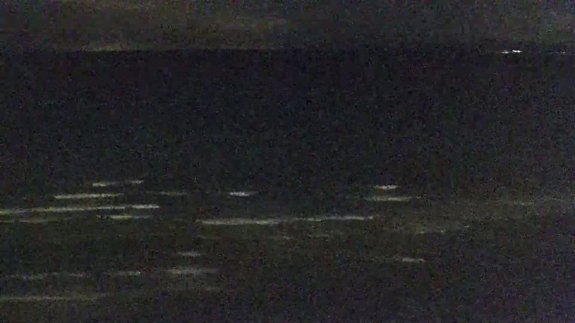 A dark, nighttime ocean scene shows small, bright patches of light on the water's surface.