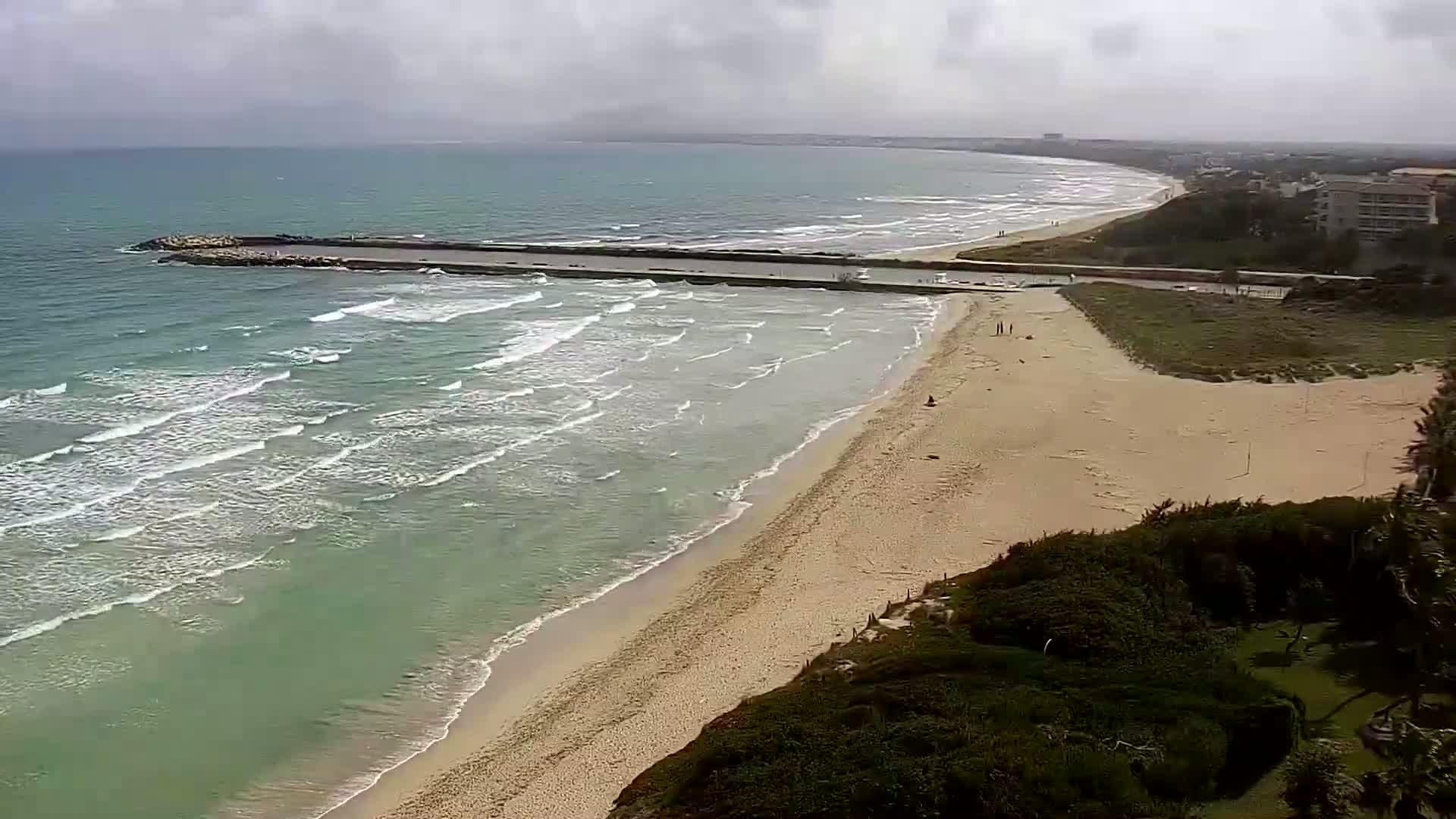 A long sandy beach with gentle waves rolls onto shore under an overcast sky.