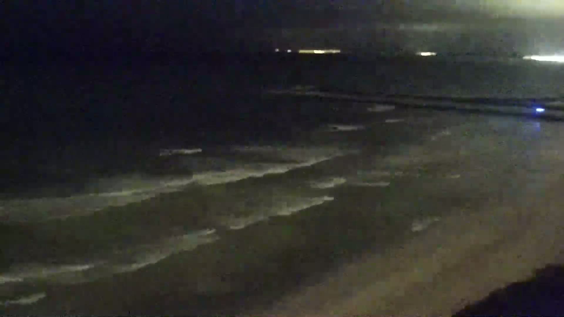 A nighttime view of ocean waves lapping a sandy shore under a dark sky.
