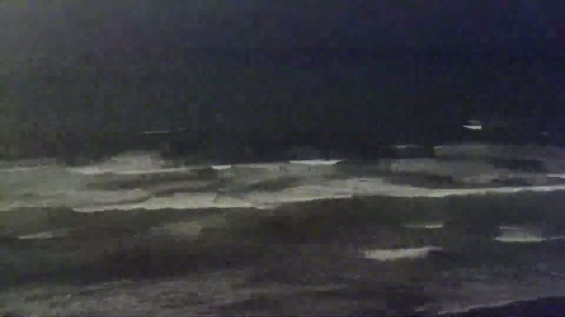 Dark, choppy waves crash on a beach under a nighttime sky.