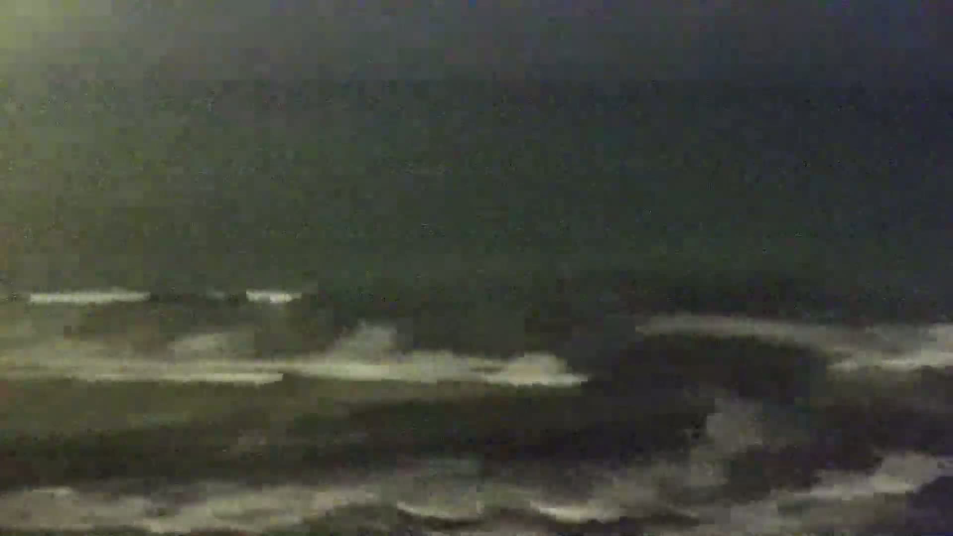 A dark, stormy ocean with choppy waves is visible at night.