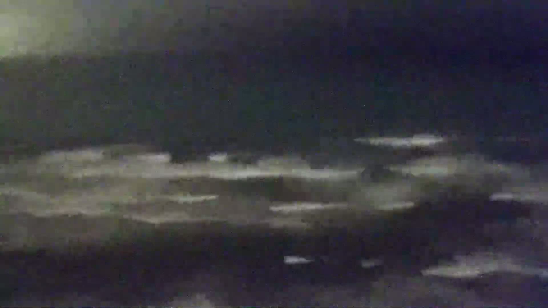 A dark, possibly nighttime, scene depicts a body of water with small waves under a cloudy sky.