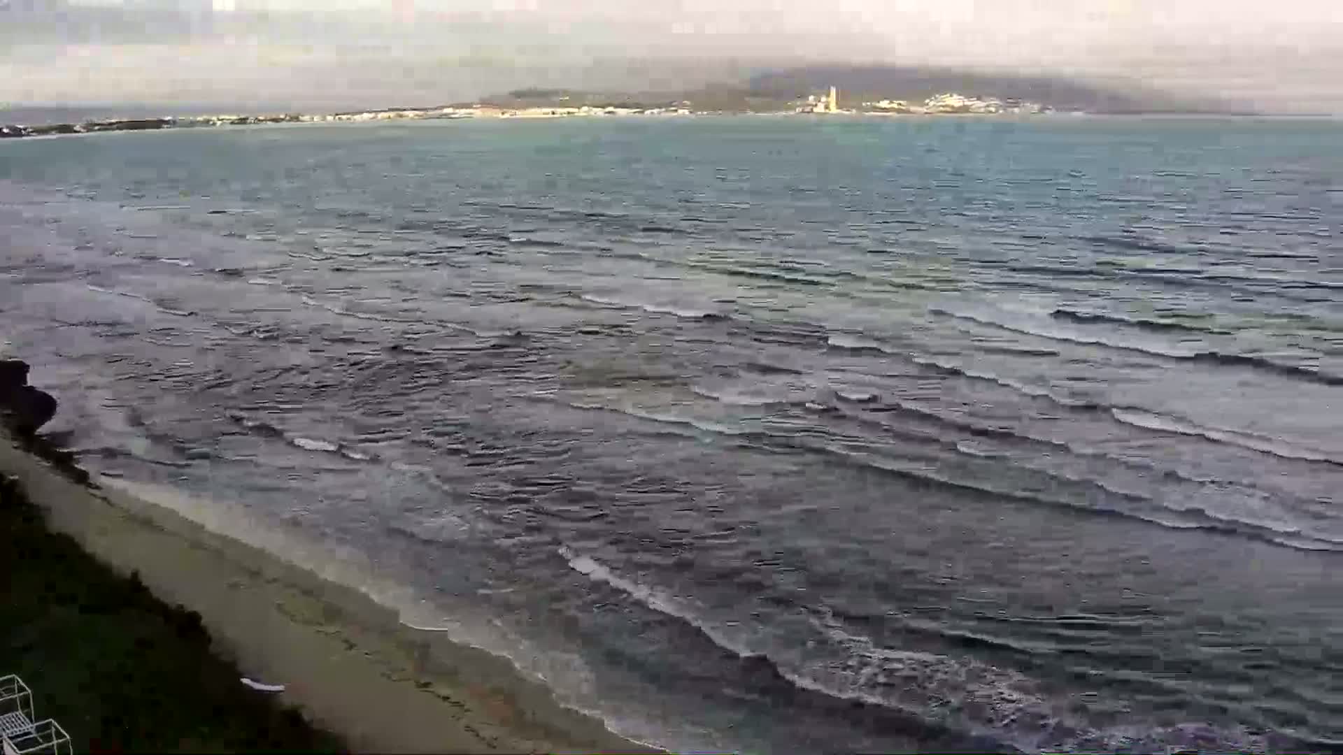A sandy beach and calm, dark-grey ocean meet under an overcast sky with a distant hazy coastline visible.