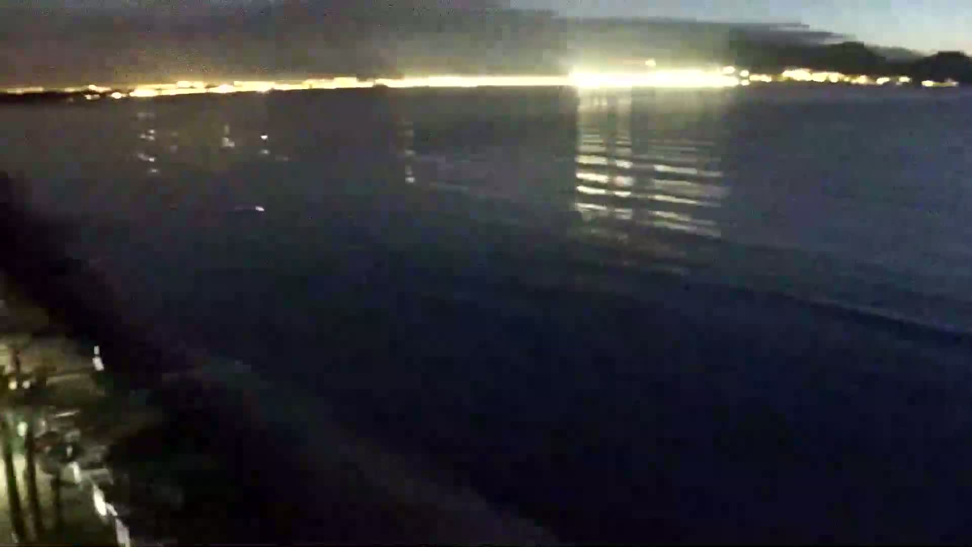 A dark body of water reflects the lights of a distant city at night.
