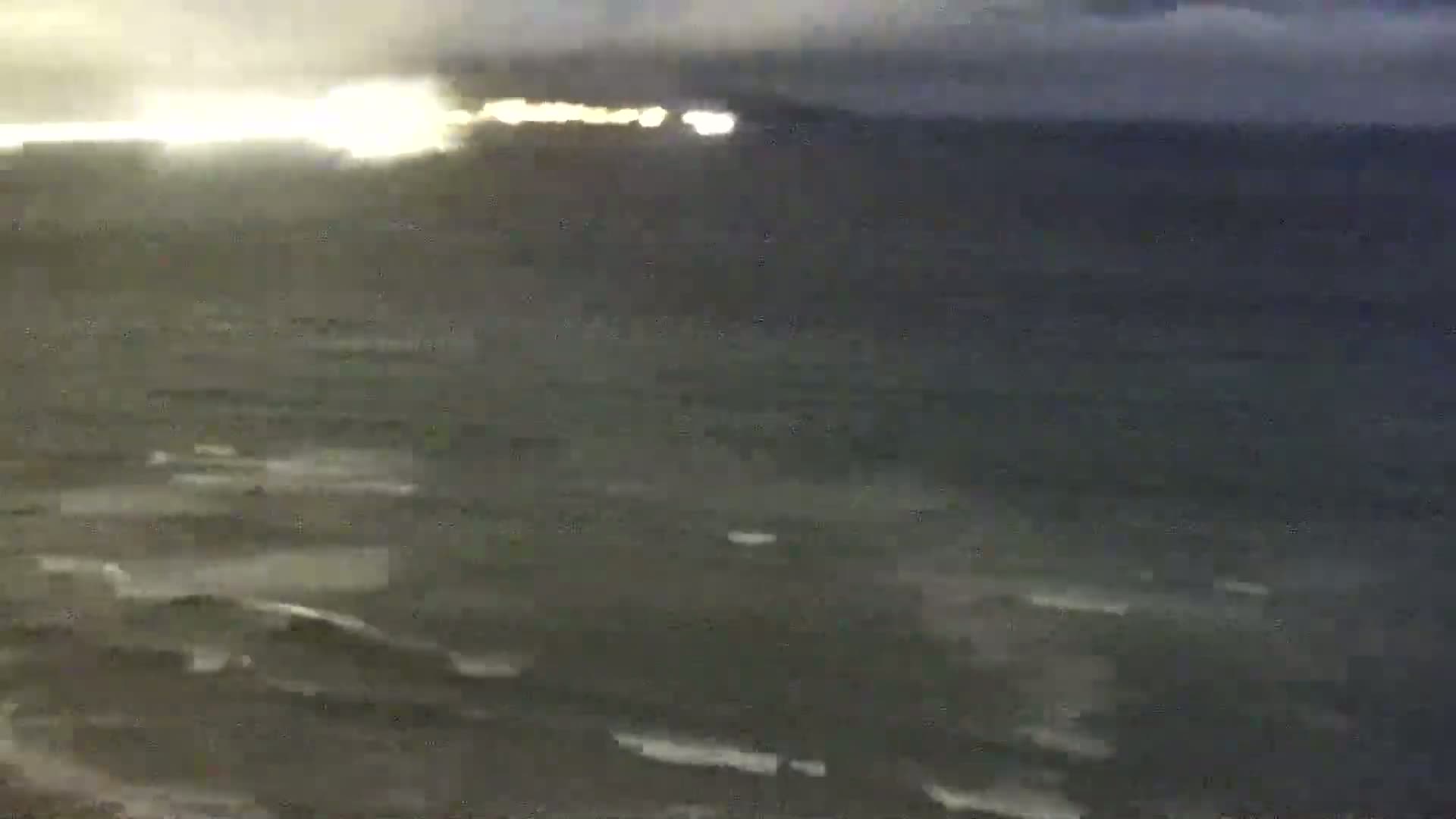 A dark, choppy sea is visible under an overcast sky, with a faint, distant glow on the horizon.