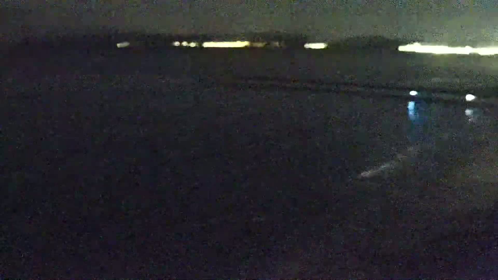 A dark, nighttime scene shows a body of water reflecting distant lights under a clear sky.