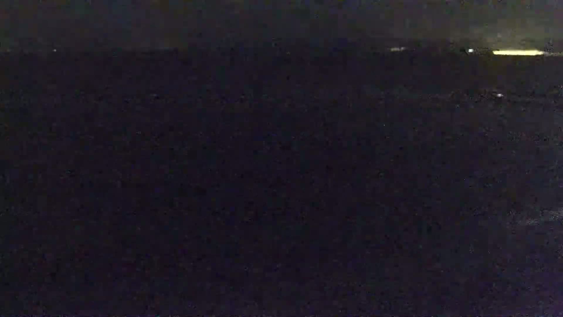 A dark, nighttime image shows a mostly indistinct, dark landscape with a faint, horizontal line of light in the distance.