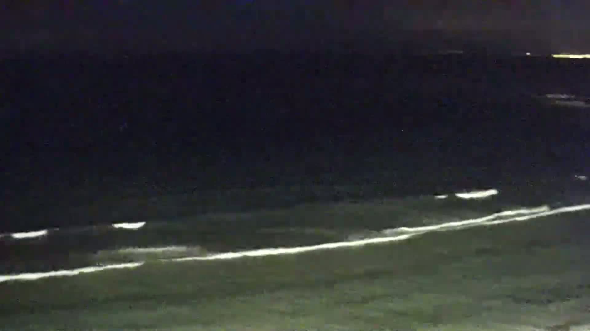 At night, gentle waves break on a dark shoreline under a clear, dark sky.