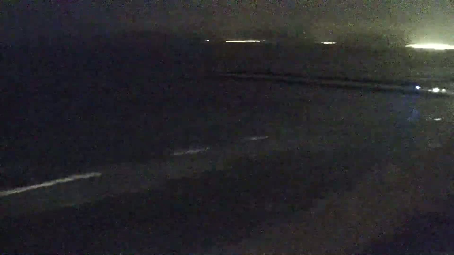 A dark, nighttime view of a roadway with faint light sources in the distance.