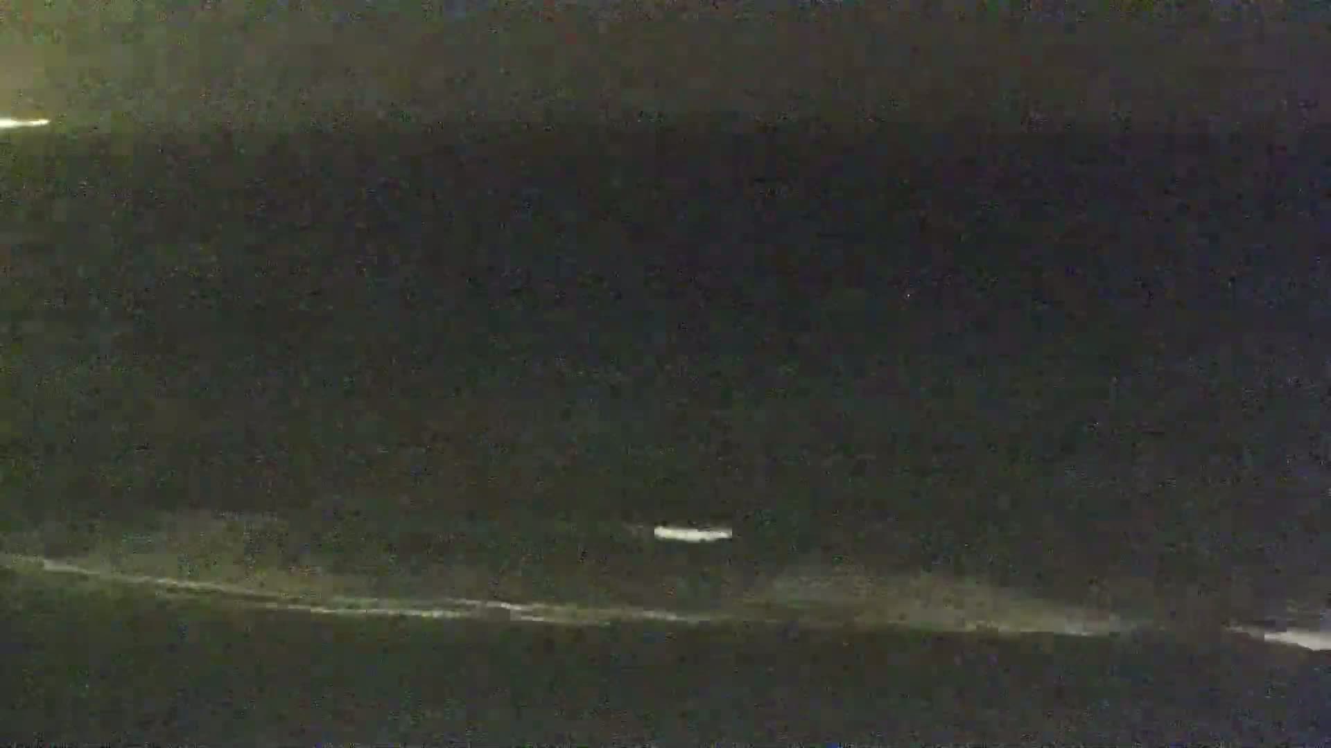 A nighttime, low-light image shows a dark body of water with a faint white line at the horizon and a small, indistinct white object in the middle distance.