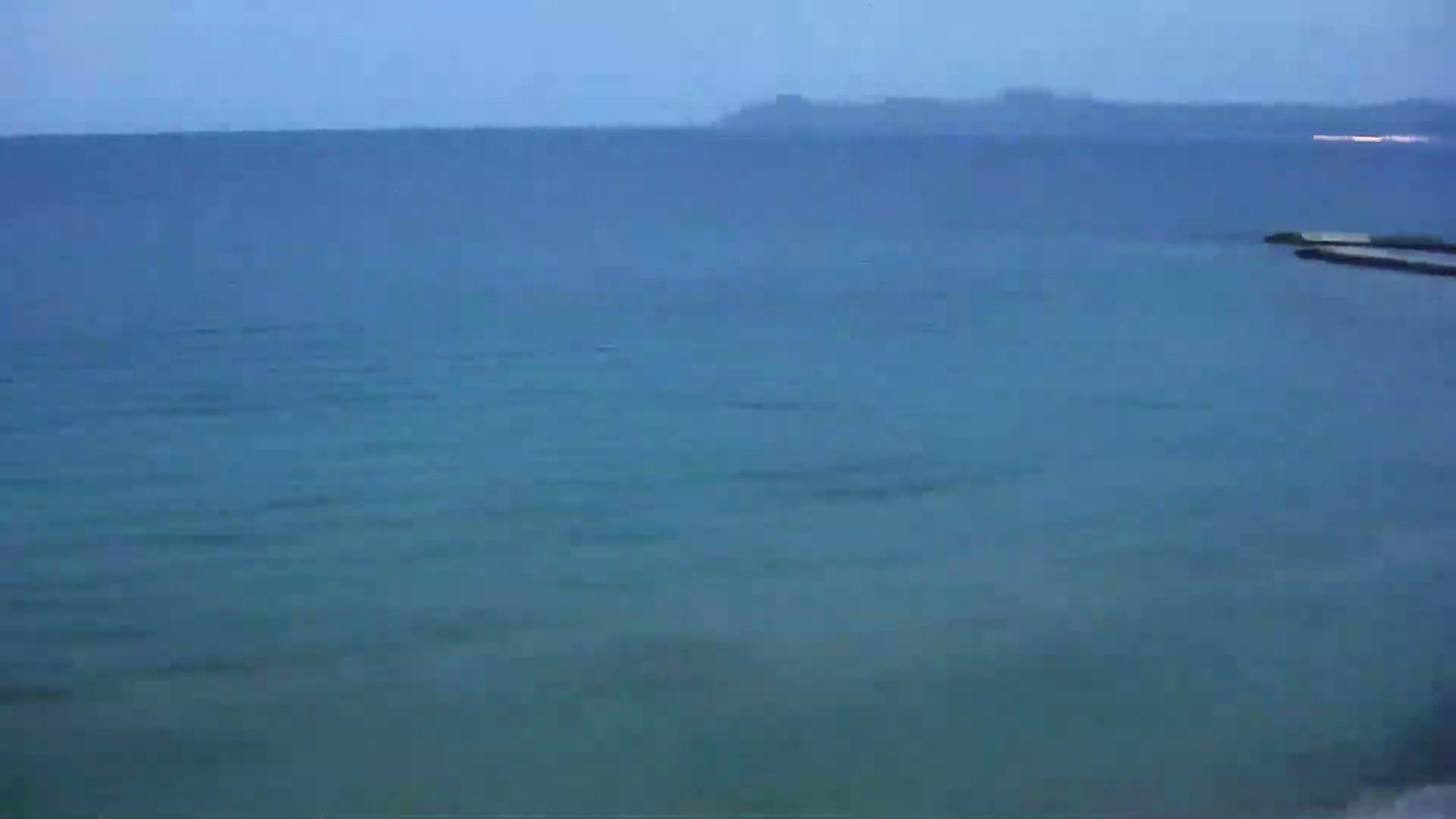 A calm, blue sea stretches to a distant, hazy shoreline under a clear, dusky sky.