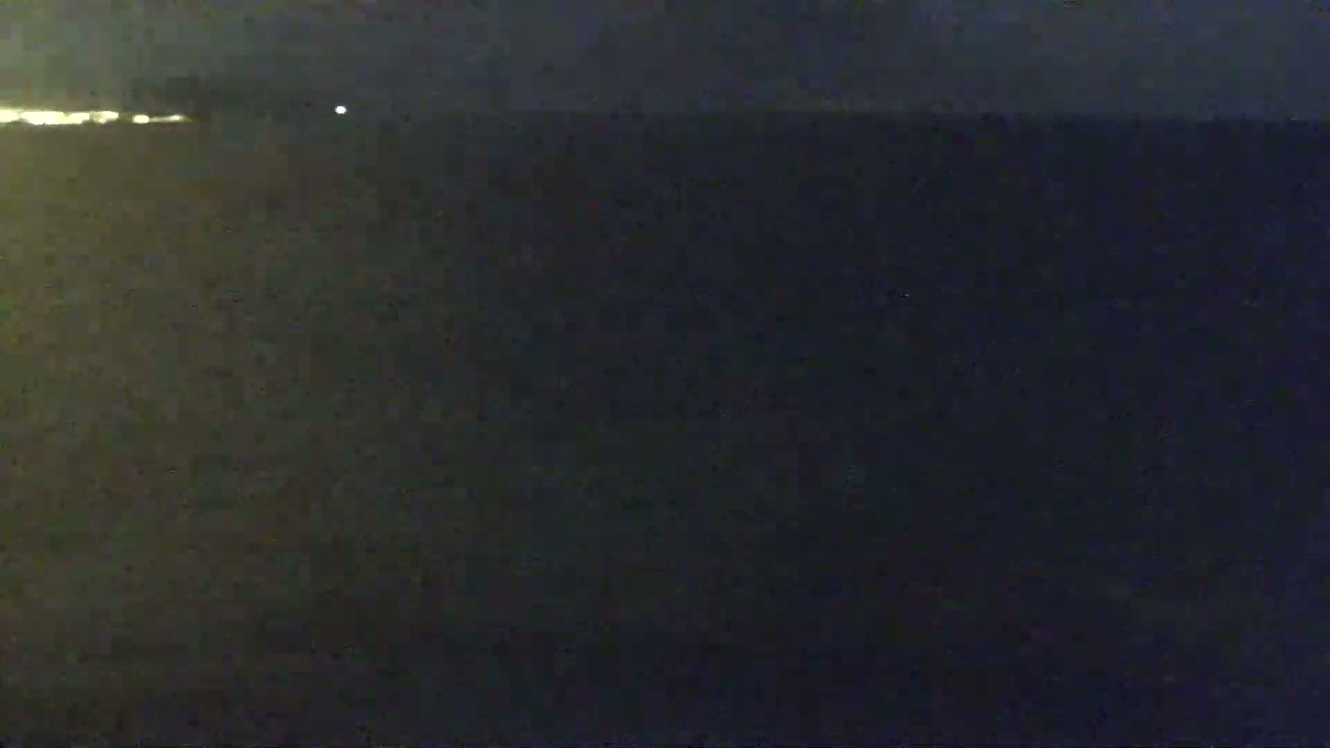A dark, nighttime scene shows a body of water with a faint light source on the horizon.