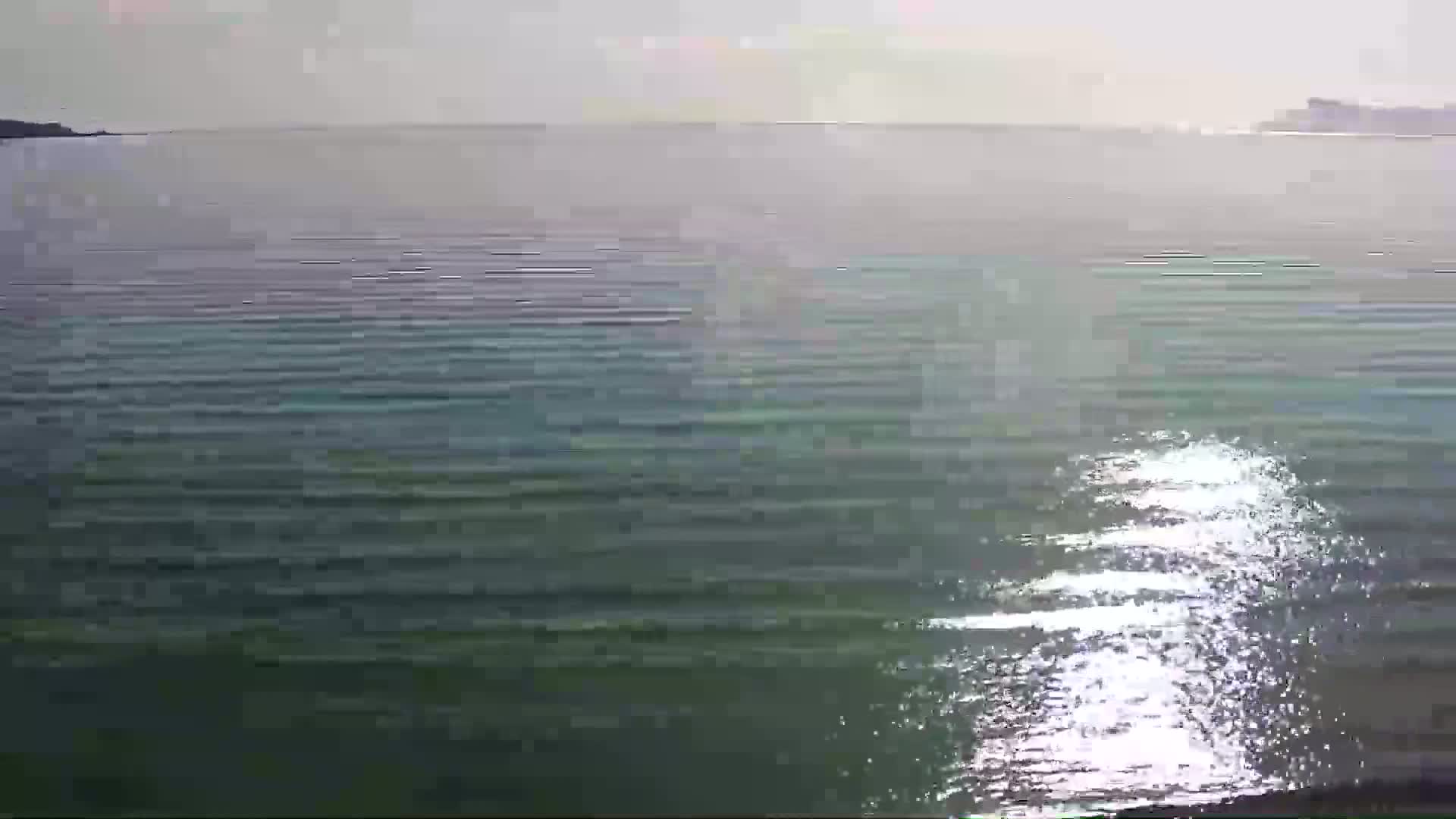 Calm, sunlit water stretches to a hazy horizon where land is visible in the distance.