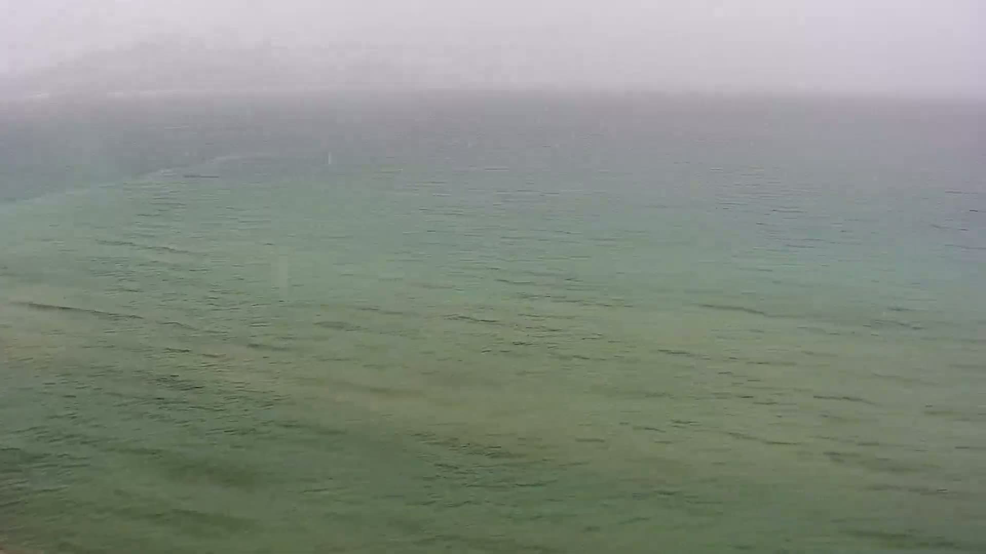 A hazy, overcast day shows a calm, greenish-grey sea with small waves.