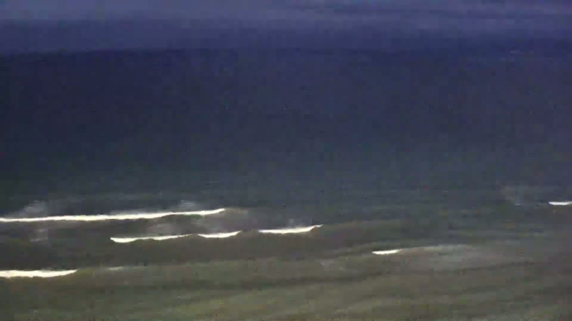 A long shot shows dark-colored water with small waves under a dark sky.