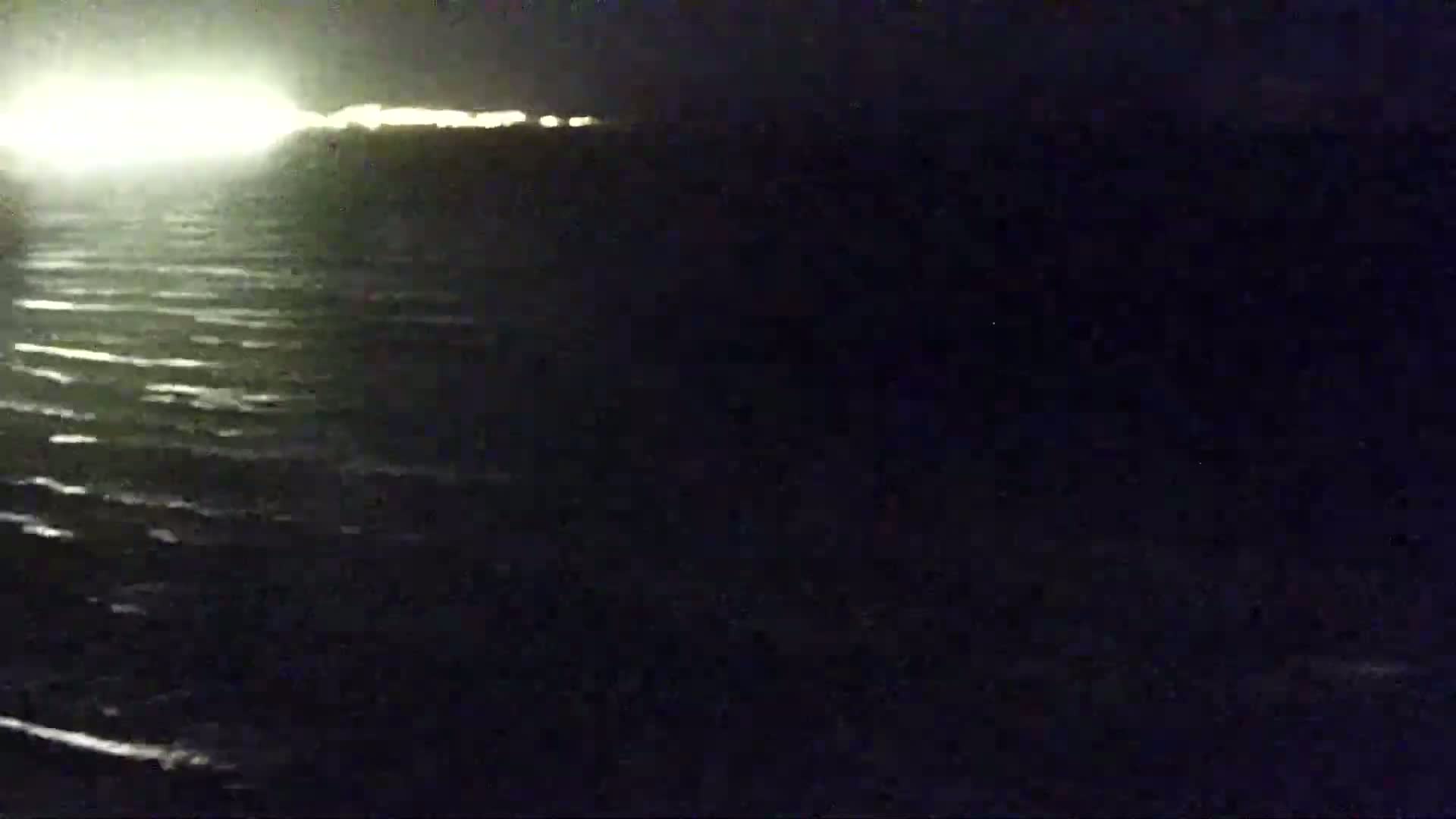 A dark body of water with small waves is visible at night, illuminated by distant lights on the horizon.