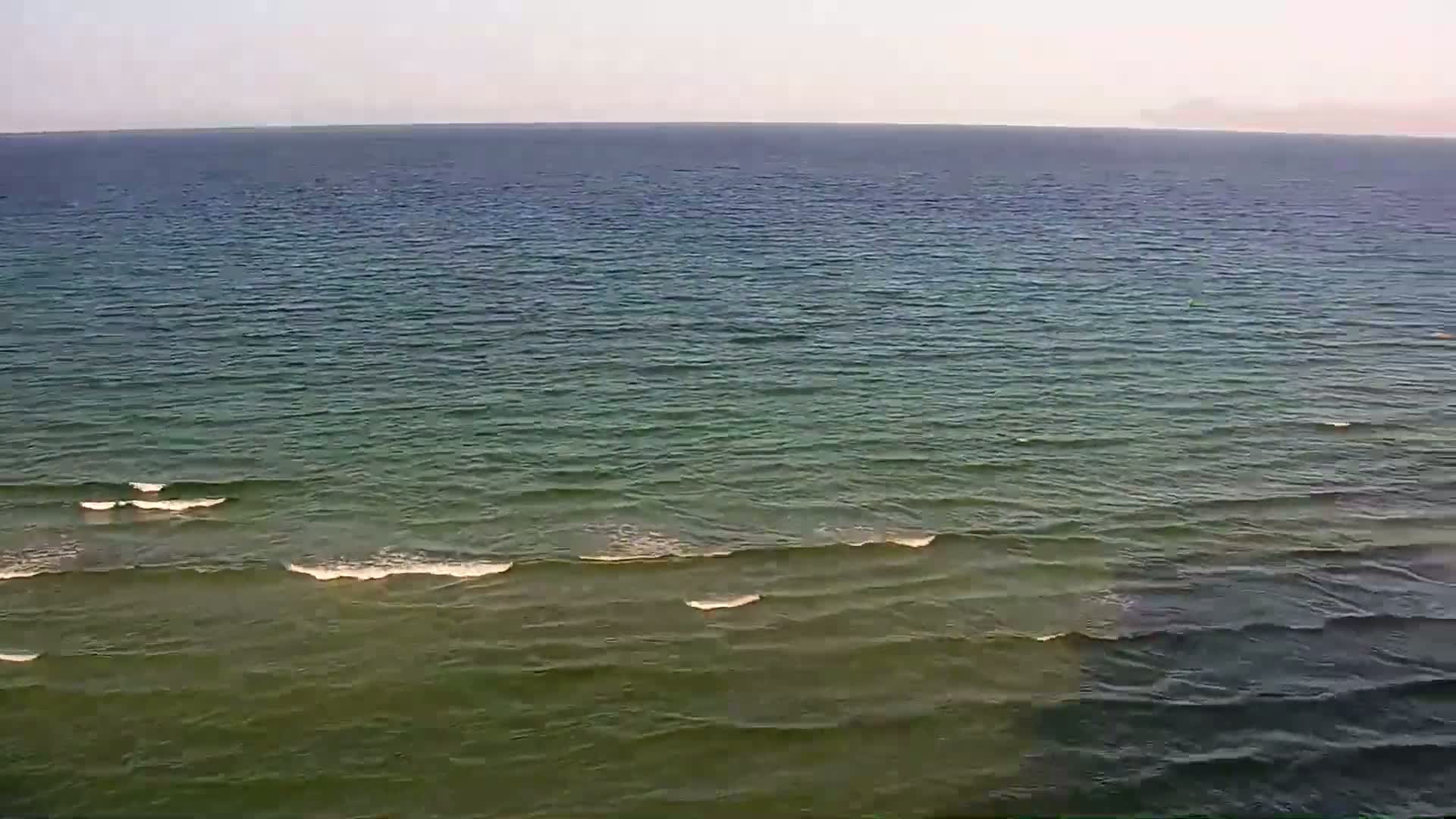 A wide expanse of relatively calm ocean water with small waves under a clear, light sky.