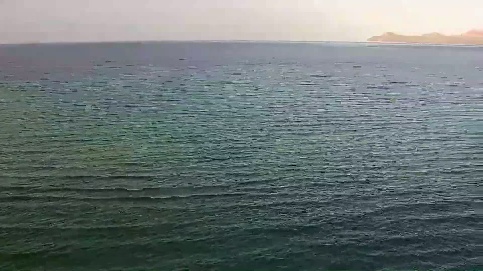 A body of dark, wavy water stretches to a distant, hazy shoreline under an overcast sky.