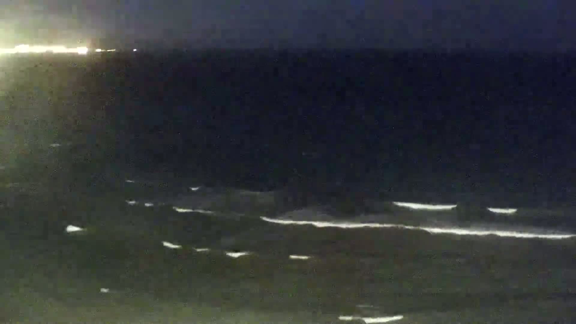 A dark, nighttime ocean scene shows gently rolling waves under a clear, dark sky.