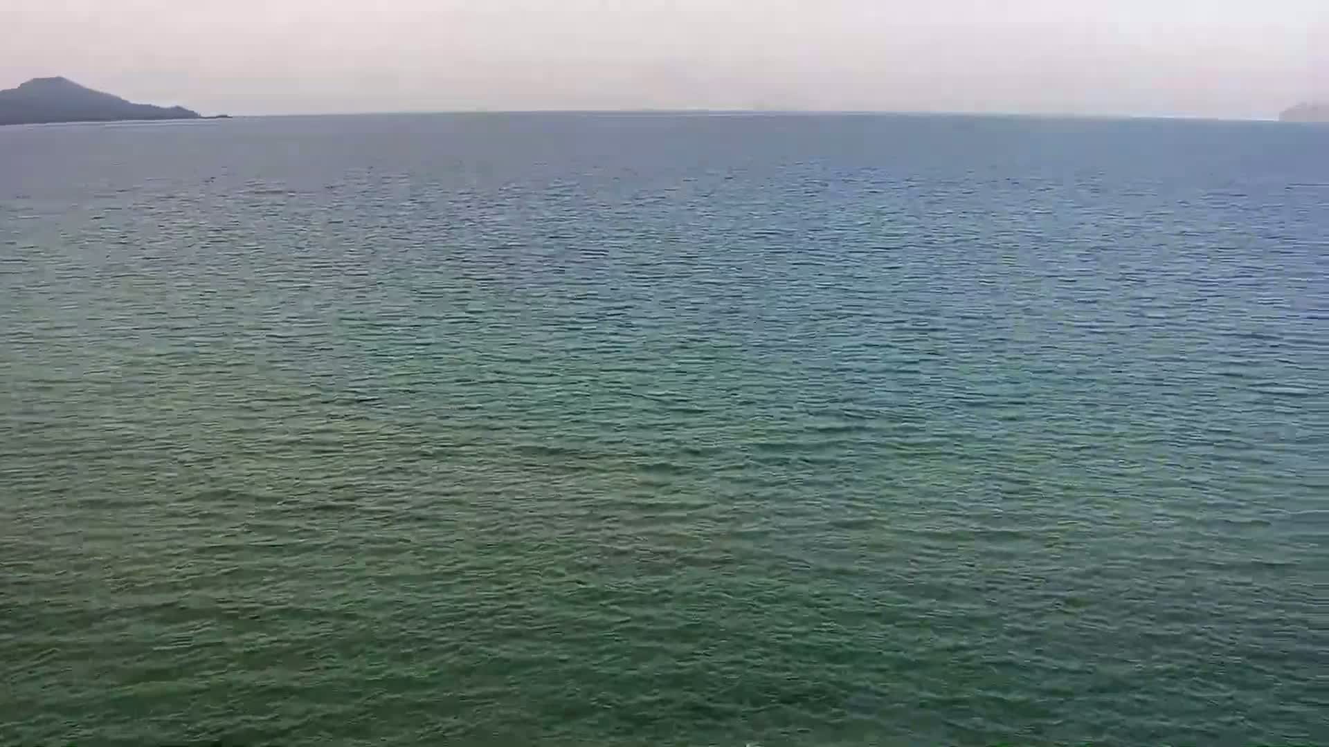 A calm, gray-sky day shows a body of dark-green water with a distant, low-lying landmass on the horizon.