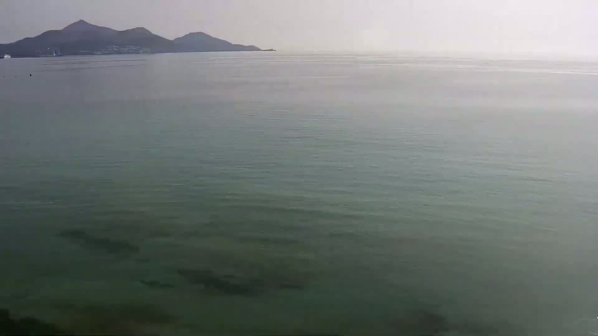 A calm, hazy body of water stretches to a distant, mountainous shoreline.