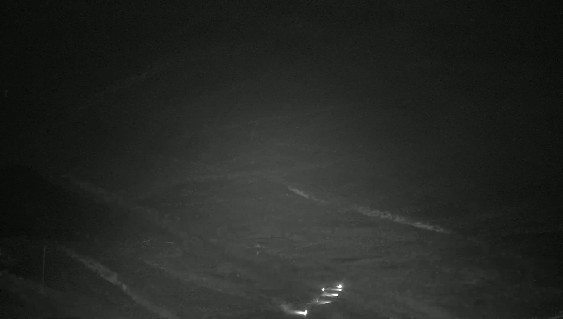 A nighttime, low-light view shows two pairs of headlights traveling on a dark road winding through a hilly landscape.