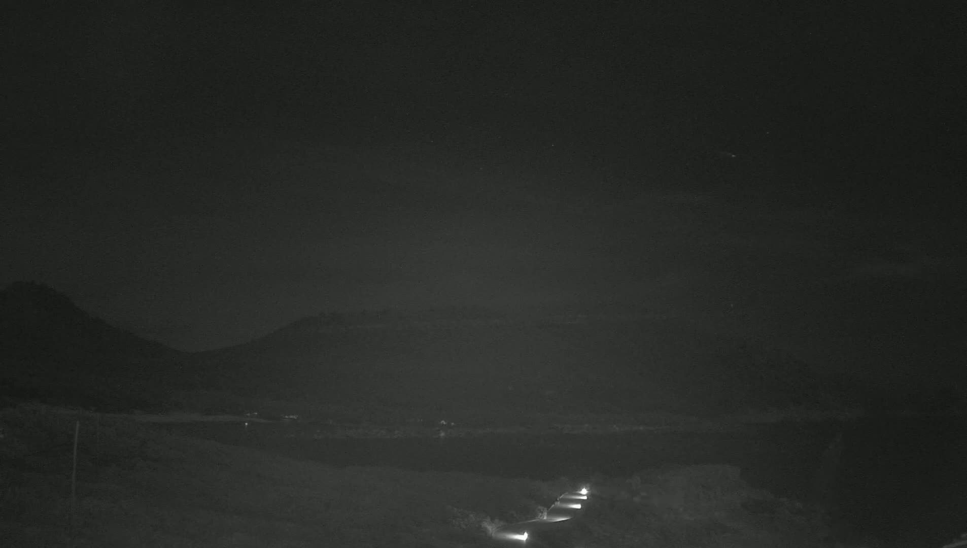 A nighttime view of a road winding through a dark landscape with hills in the background under a clear sky.
