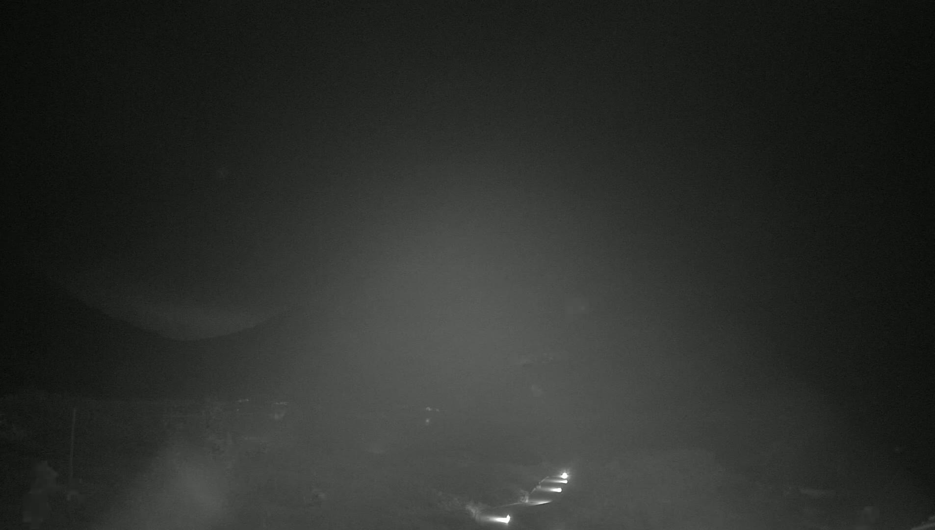 A nighttime, foggy landscape is visible, with faint lights from what appears to be a roadway in the lower portion of the image.