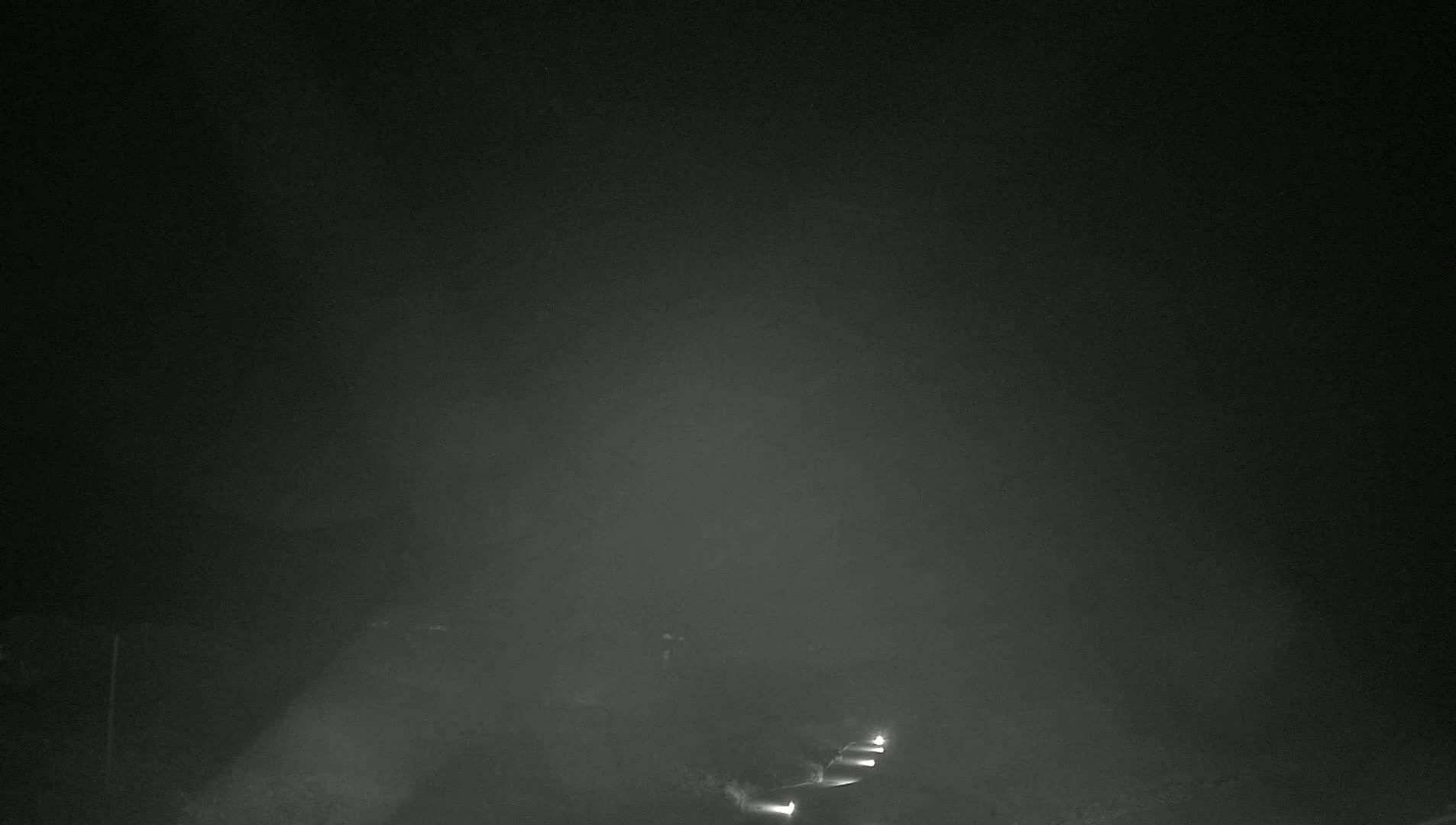 Headlights from vehicles are visible in the distance through a heavy fog at night.