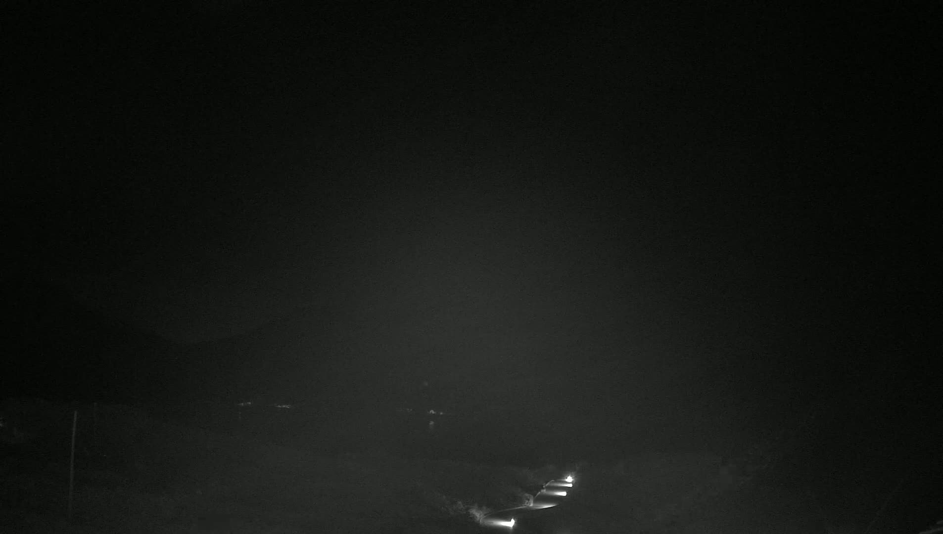 Headlights from several vehicles are visible on a dark road at night under a hazy sky.