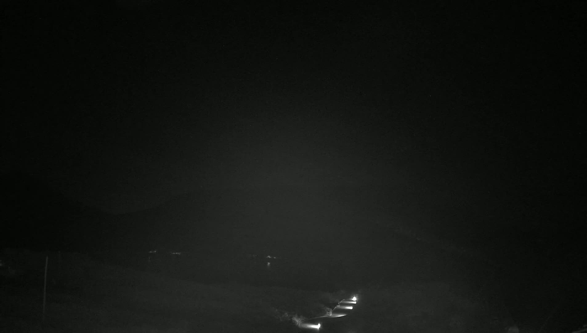 At night, a road with a few sets of vehicle headlights is visible in a hazy or foggy environment.