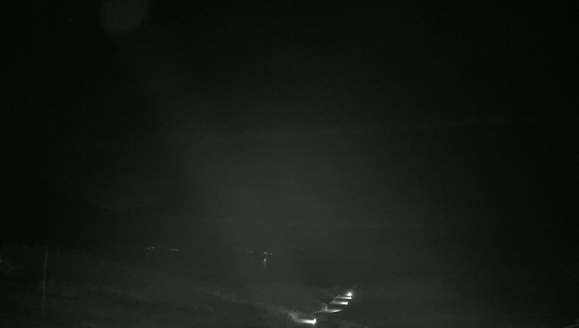 A nighttime, hazy scene shows a road with a few vehicles' headlights visible in the distance.