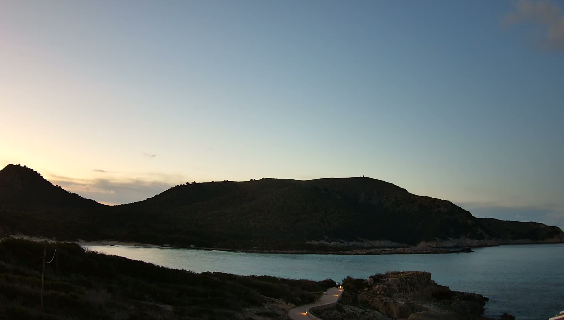 A calm bay is nestled between two dark, tree-covered hills under a twilight sky.