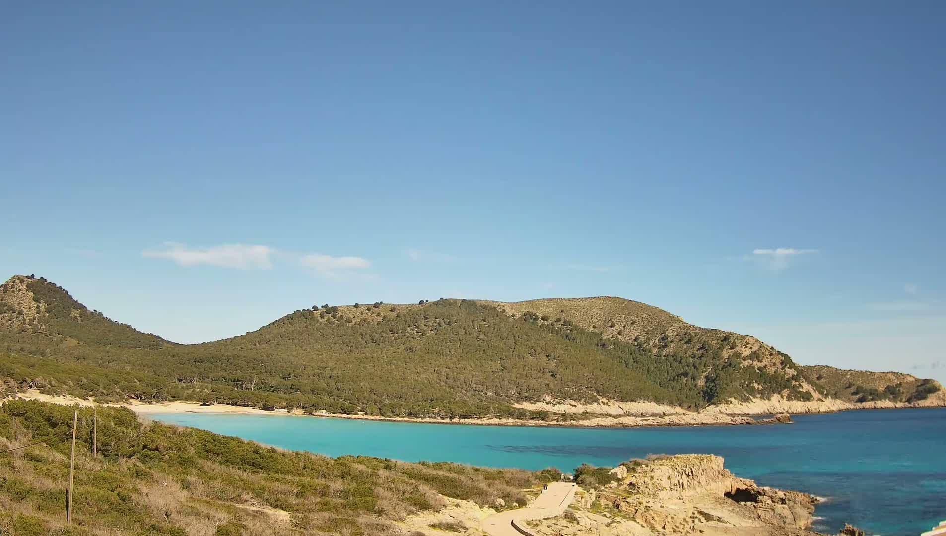 A secluded turquoise cove nestled between two verdant hills under a clear blue sky.